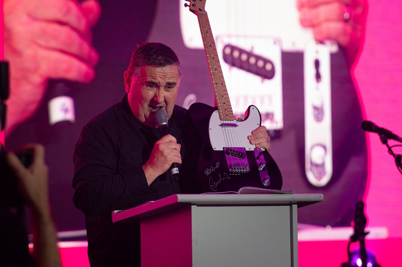 man with black shirt on stage with a mic in his hand and hand infront of him
