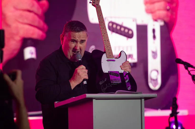 man with black shirt on stage with a mic in his hand and hand infront of him