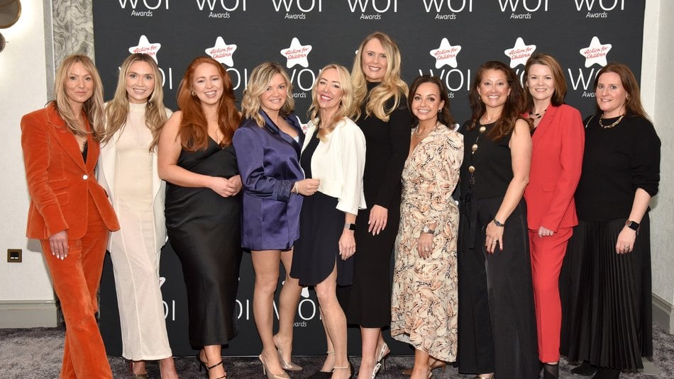 Ten smartly dressed women lined up in front of a Women of Influence Screen, smiling at the camera
