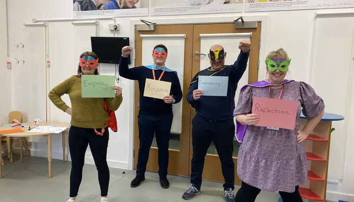 Four Action for Children Young Person's Practitioners from the Blues Programme wearing dressed as superheros holding cards that read - empthay, kindness, empowering and reflection