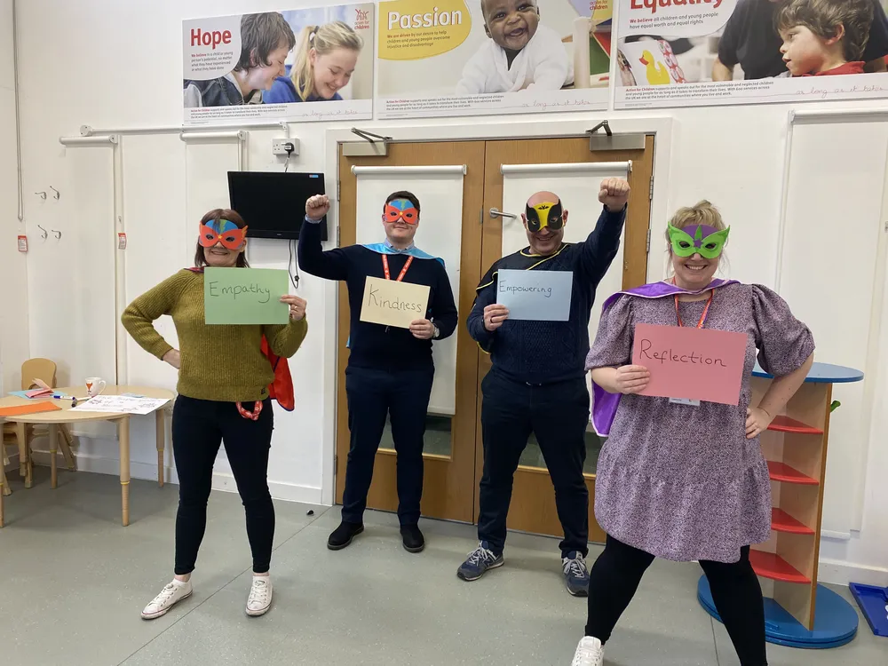 Four Action for Children Young Person's Practitioners from the Blues Programme wearing dressed as superheros holding cards that read - empthay, kindness, empowering and reflection