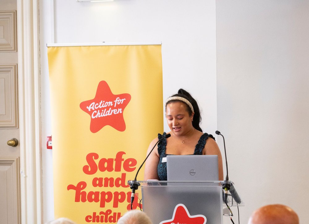 Young woman speaks at a microphone stand in front of a yellow backdrop