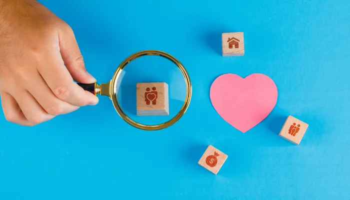 Family concept with paper cut heart on blue table flat lay. hand holding magnifying glass over wooden cube.