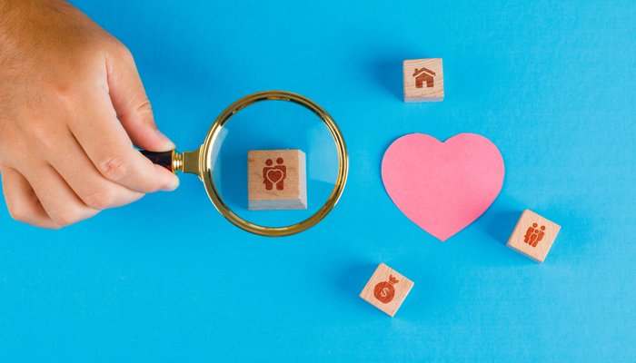 Family concept with paper cut heart on blue table flat lay. hand holding magnifying glass over wooden cube.