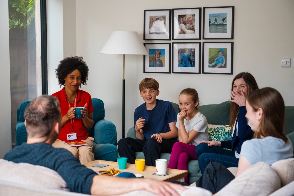 Warm initial fostering visit with a social worker and a family sharing laughter around the table