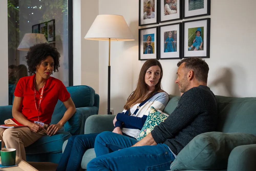 Social worker giving guidance to two foster parents on a sofa, showing support through the fostering process