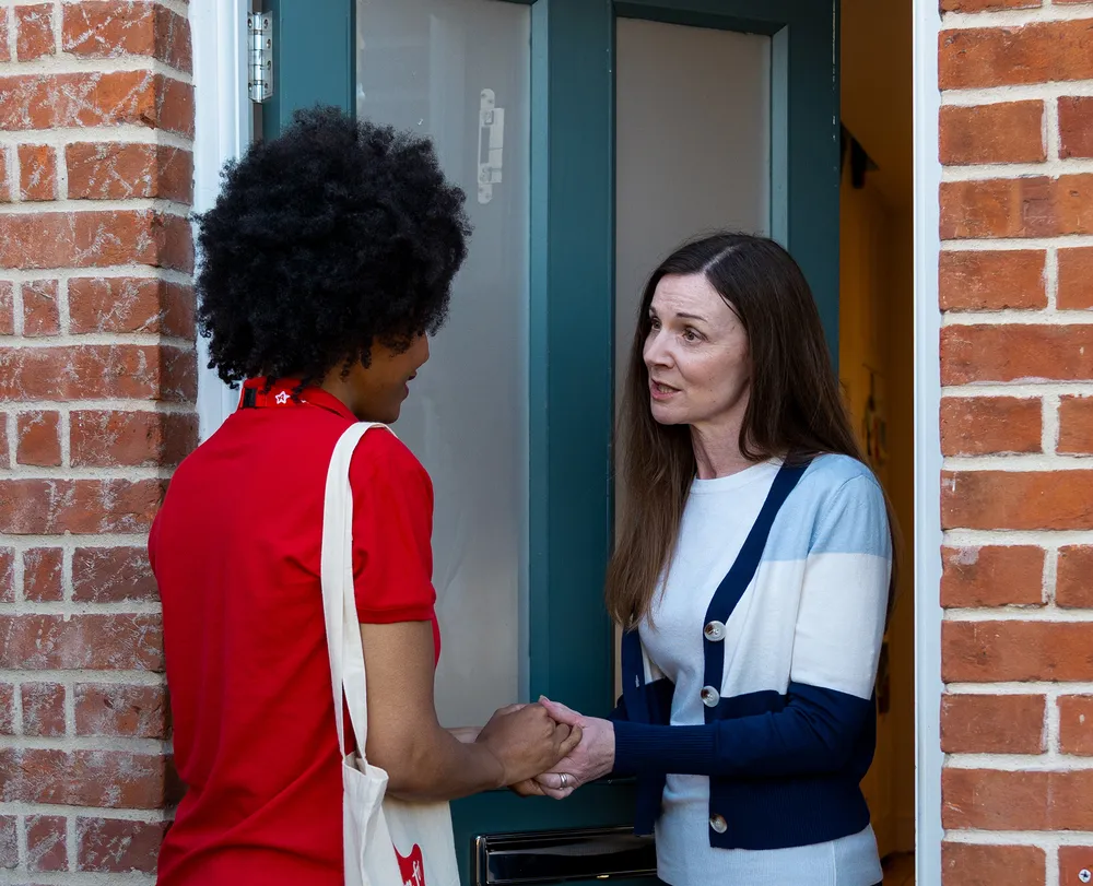 Social worker holding a carer’s hand at the door, offering reassurance during a fostering transfer