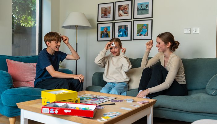Two older teens playing a board game with a younger foster child, showing fun and connection in fostering in Scotland