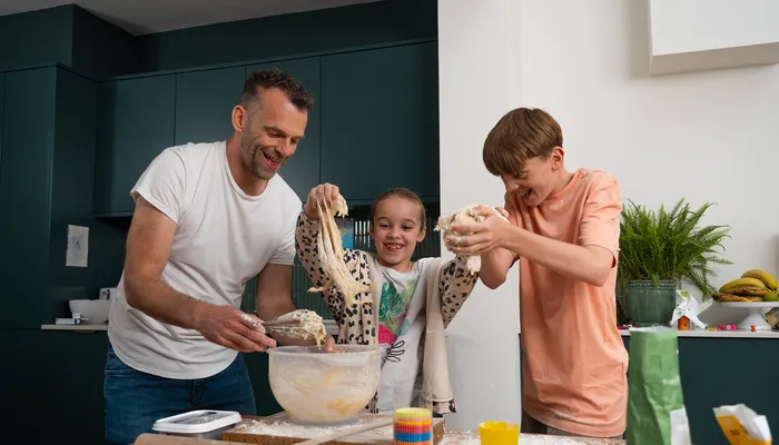 Two foster children smiling and playing with dough alongside their carer during a fun baking activity