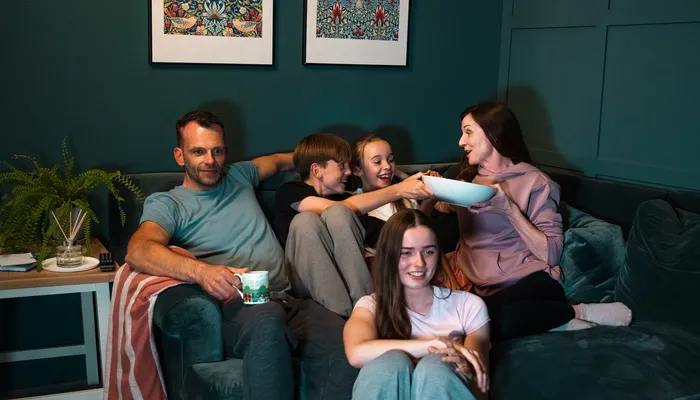 Family watching a movie with two foster children, sharing popcorn and showing everyday fostering life