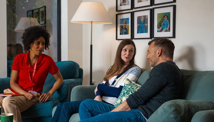 Social worker giving guidance to two foster parents on a sofa, showing support through the fostering process