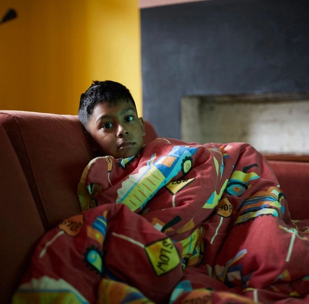 Boy looking into the camera with a worried face covered by a blanket