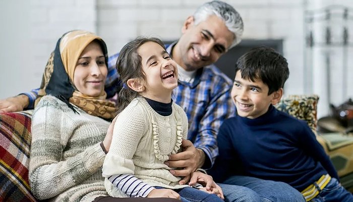 Muslim foster carers cuddling and playing with two siblings, showing a loving and inclusive foster home