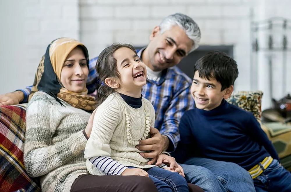 Muslim foster carers cuddling and playing with two siblings, showing a loving and inclusive foster home