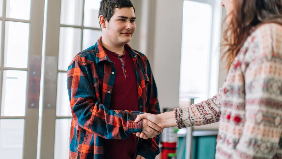 A young female social worker greeting and shaking hands with a young teenage boy