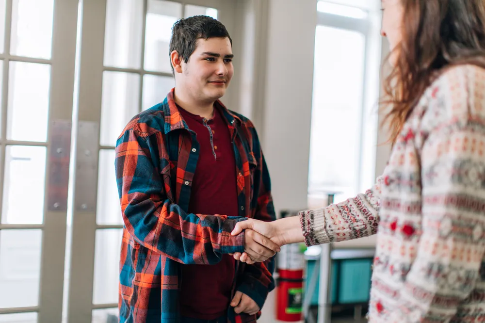 A young female social worker greeting and shaking hands with a young teenage boy