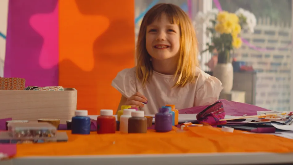 Abby, a young girl, looking up from her finger painting with a smile on her face