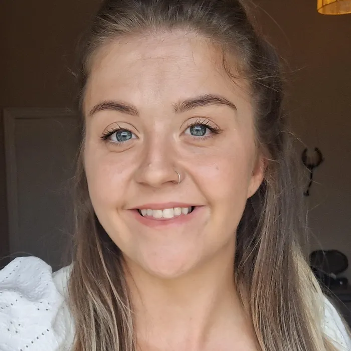 A headshot of a smiling young woman with a nose piercing