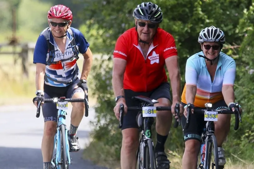 Three people on cycling. Person in the middle is wearing an Action for Children cycling t-shirt