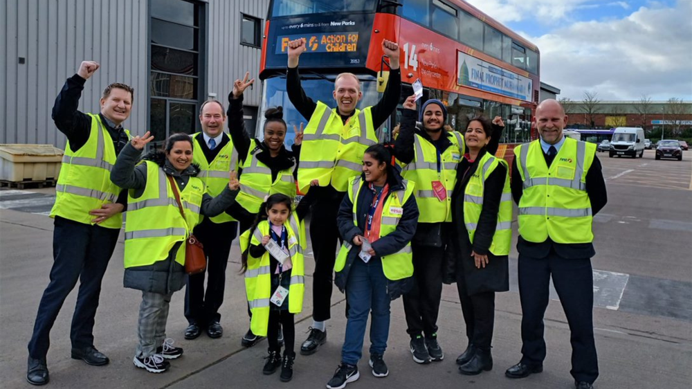 Action for Children Young Ambassadors in hi-vis vests in front of a First Group bus