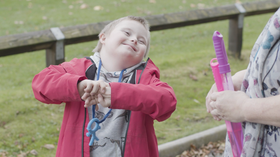 Alfie, A young boy with Down Syndrome smiling at a person to the side of the shot