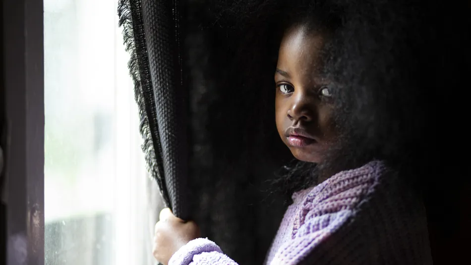 Alice, a sad young girl stands at the window while looking into camera