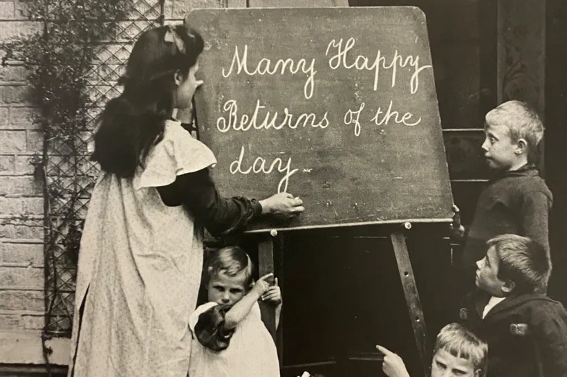 Black and white photograph of children writing on a chalk board
