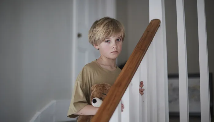 Boy standing on stairs holding teddy looking sad