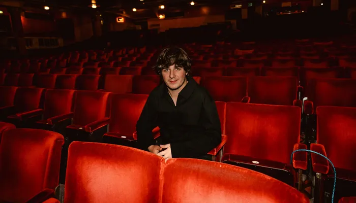 Brad Kella sitting in a chair within a theatre