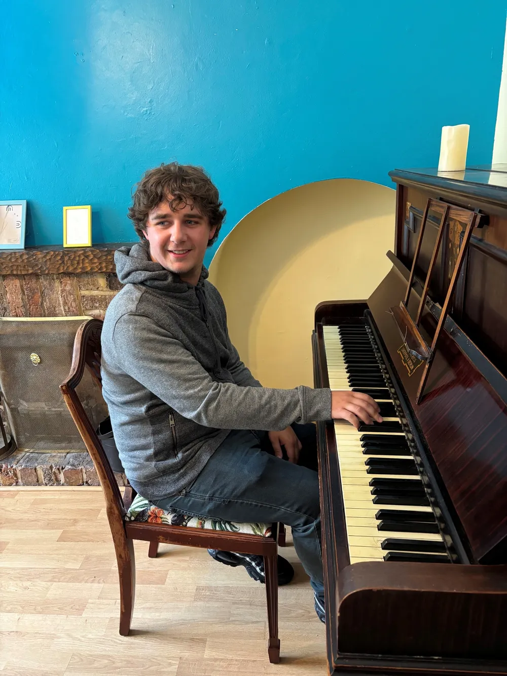 Brad Kella sitting at an old piano in someone's front room