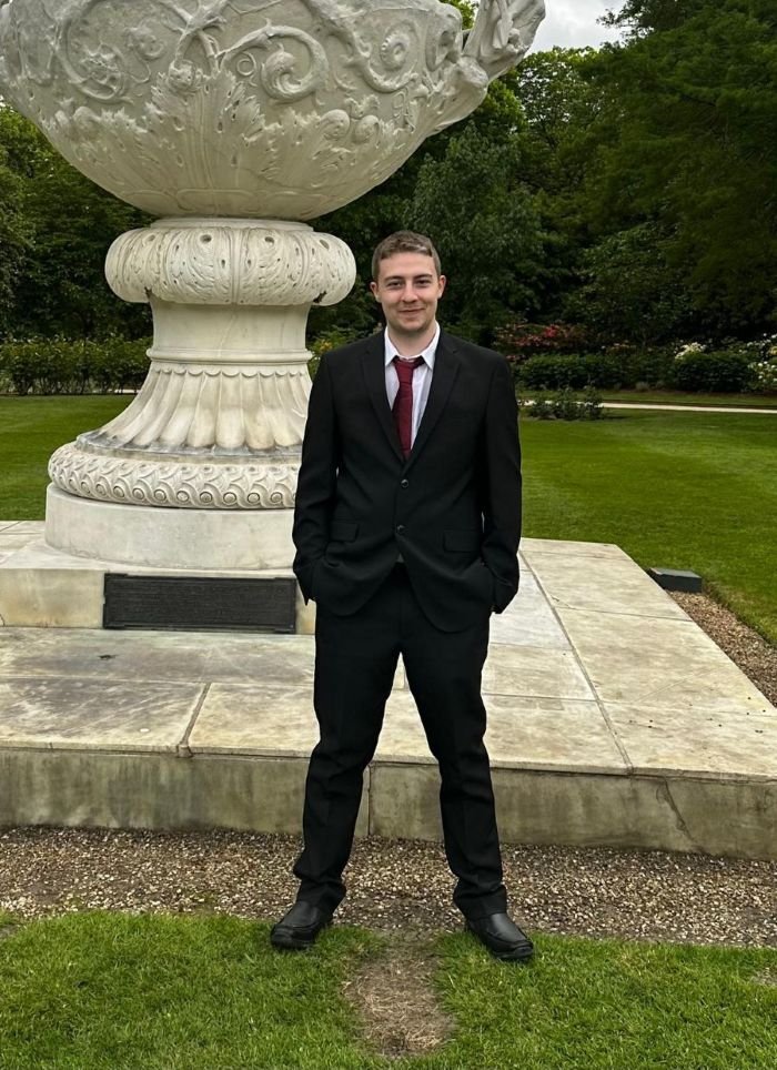 A photo of a young person we've supported. He is wearing a black suit and smiling at the camera.