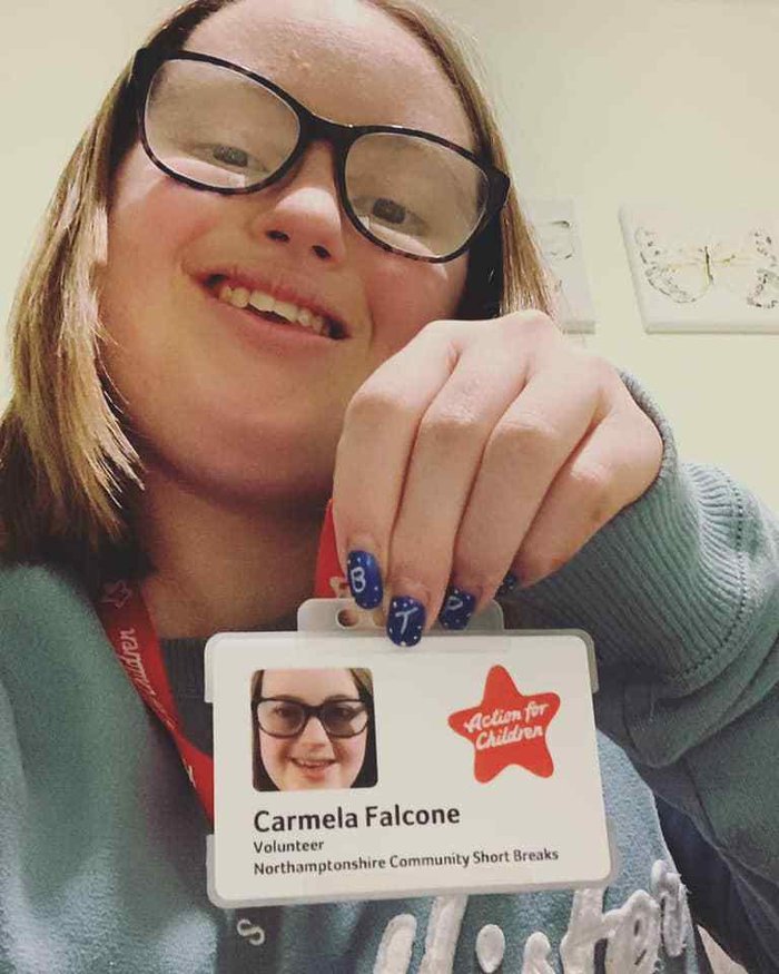 Carmela takes a selfie. She is smiling and holding up her Action for Chldren Volunteer badge