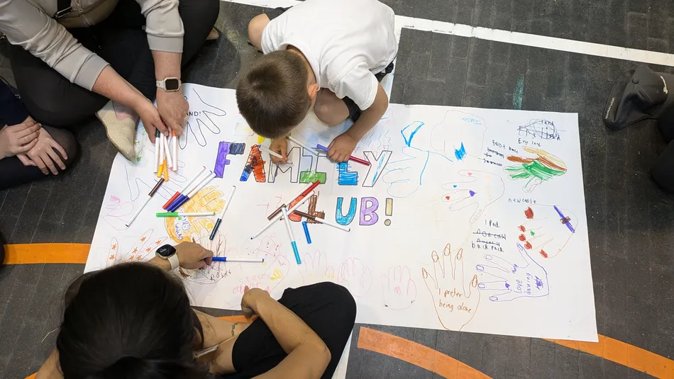 Children drawing the words family club on a big piece of paper on the floor