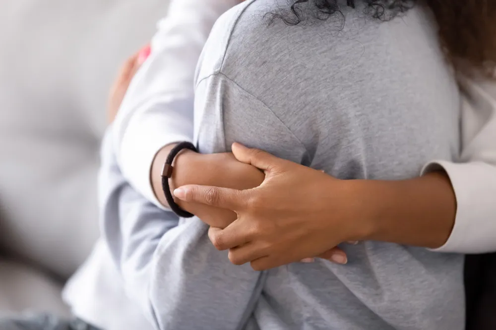 Close up shot of a woman hugging a young girl. The young girls arms are wrapped tightly around the woman's back