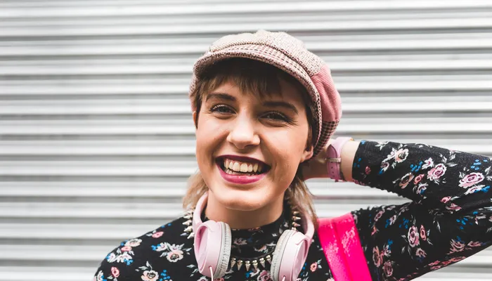Colourfully dressed teenage girl standing against a metal shutter and smiling at the camera
