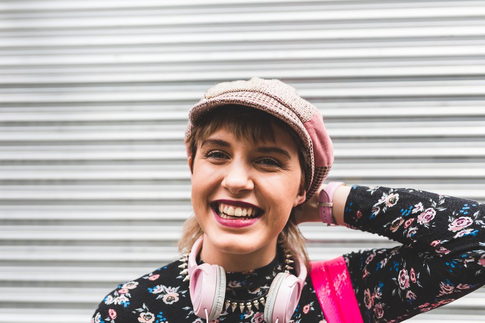 Colourfully dressed teenage girl standing against a metal shutter and smiling at the camera