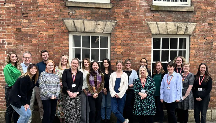 A happy team huddled for a group photo in front of a redbrick building.