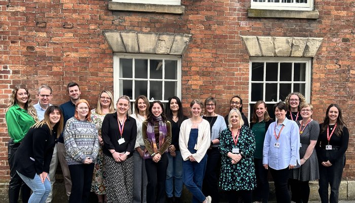 A happy team huddled for a group photo in front of a redbrick building.