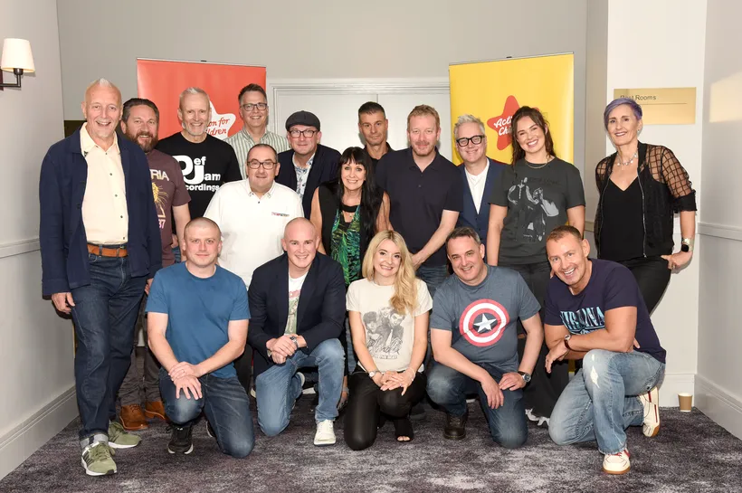 17 smiling adults posing in a carpeted venue in front of Action for Children pull up banners