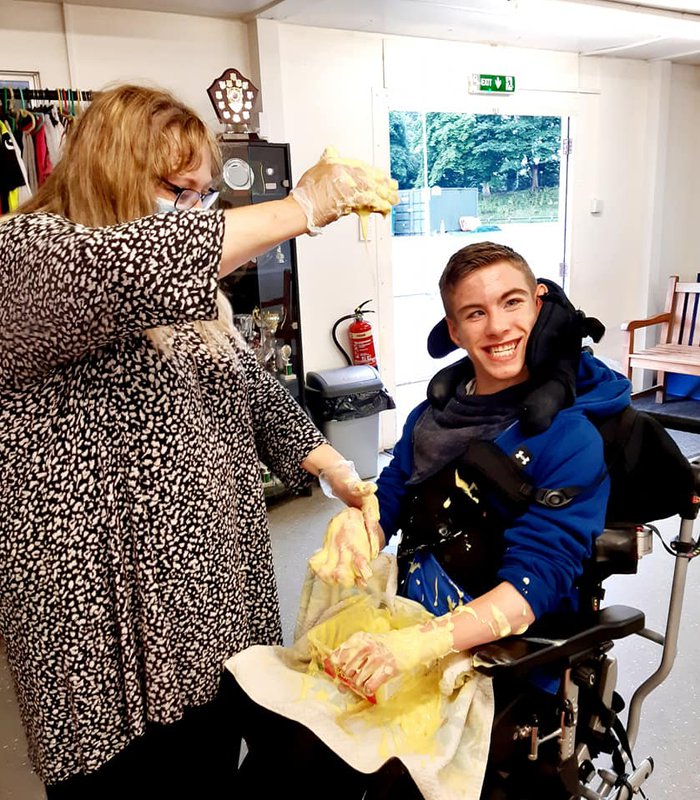 Debra and a young boy in a wheelchair playing. A small box of wet sand is played on the young boys lap and both their hands are messy..jpg