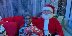 A young boy sitting in a winter grotto beside Santa holding a gift