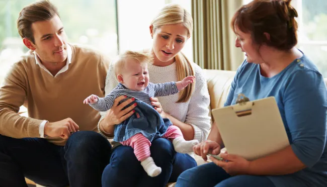 A mother looking concerned with her baby on her lap whilst speaking to a family support worker