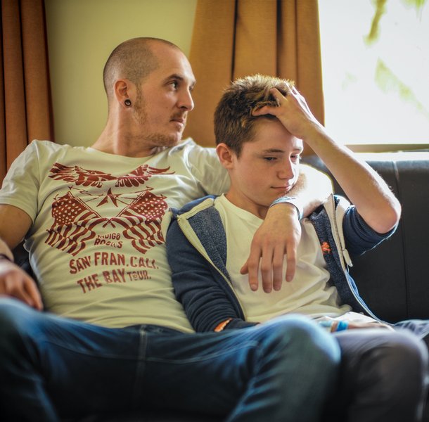 Father with arm around teenage son sitting on the sofa together