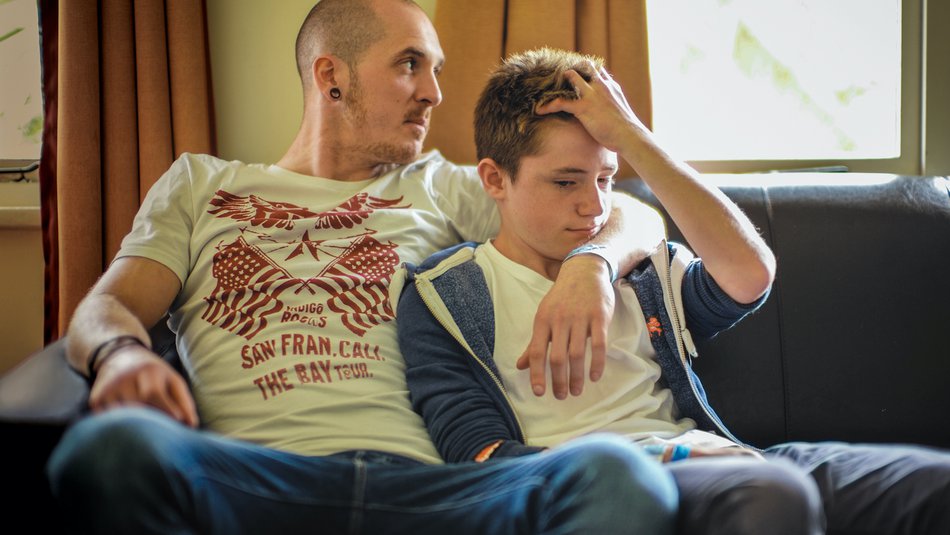 Father with arm around teenage son sitting on the sofa together