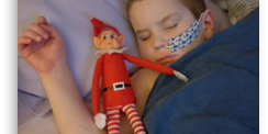 Little boy asleep with feeding tube next to Christmas elf