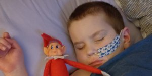 Little boy asleep with feeding tube next to Christmas elf