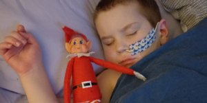 Little boy asleep with feeding tube next to Christmas elf