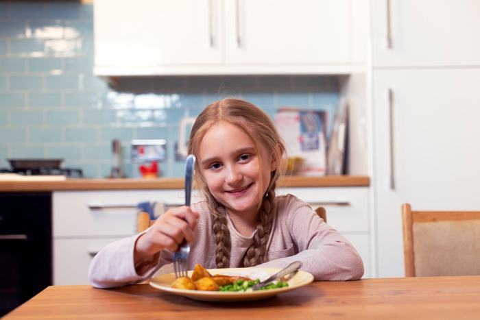 Freya sits at the kitchen table eating Christmas dinner and smiling towards the camera.