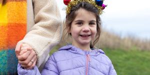 A young girl wearing a lilac winter coat with a festive headband featuring tinsel and baubles, holding an older person's hand