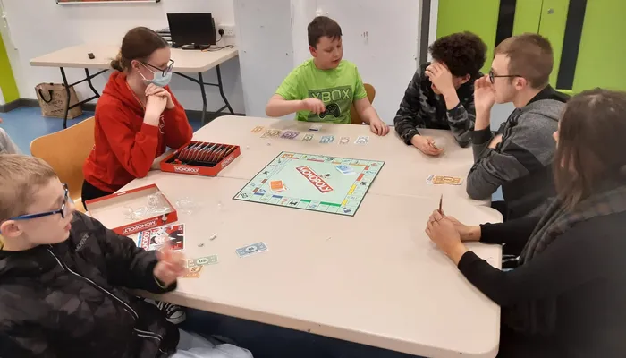 Group of children and young people sitting at a table playing monopoly